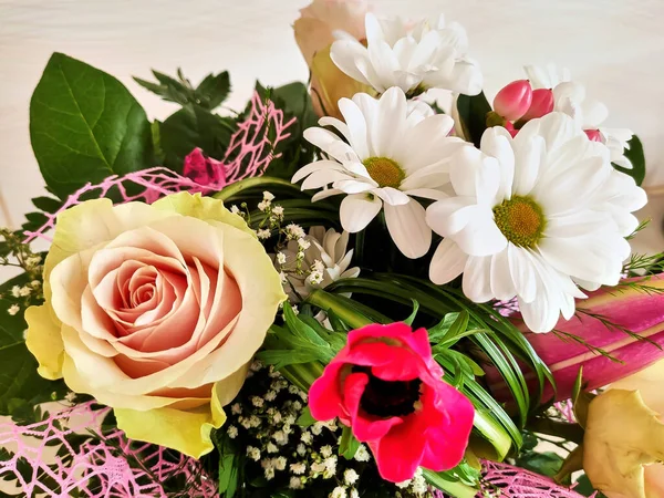 一束黄色粉红的玫瑰 白色的雏菊和红色的茴香花 绿叶和一顶粉红的装饰网 图库照片