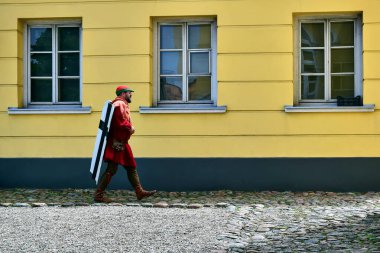Ventspils, Letonya - 06.11.2017: Müze, Livonya Düzeni kalesi, şövalye turnuvası Lilium Vindaviensis, kırmızılı ortaçağ askeri, arkasında siyah haç bulunan beyaz bir haç taşır..