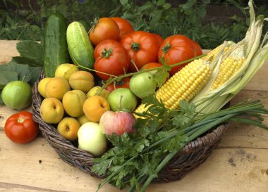 Üzüm ve yeşil yaprakların arka planında hasır bir sepette sebzeler.