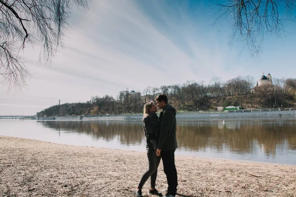 Vrolijke, liefdevolle elkaar kussen paar. Lopen op de rivier bank en omarmen — Stockfoto