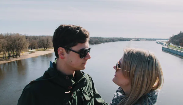 Hermosa amándose pareja está de pie en el puente sonriendo y besándose . —  Fotos de Stock