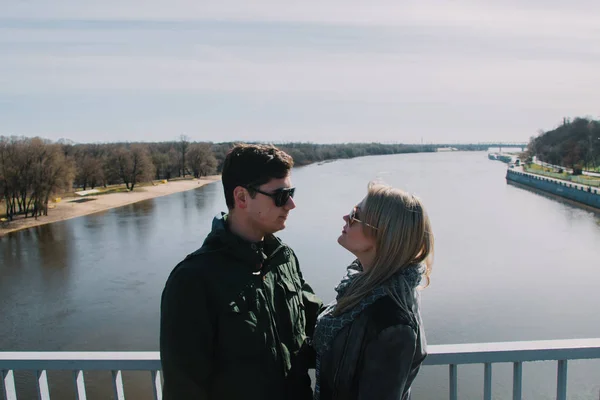 Hermosa amándose pareja está de pie en el puente sonriendo y besándose . — Foto de Stock