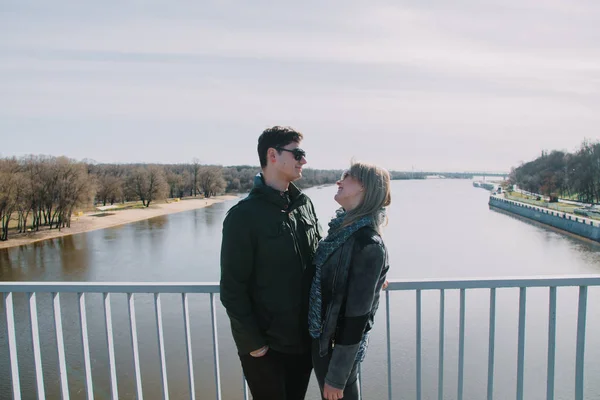 Hermosa amándose pareja está de pie en el puente sonriendo y besándose . —  Fotos de Stock