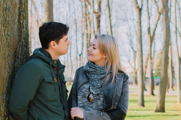 A beautiful loving couple smiling and kissing a large tree in the park. — Stock Photo, Image