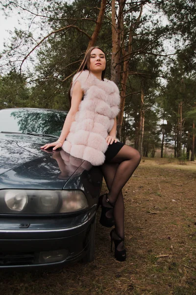 Retrato de una chica muy hermosa en un bosque vestida de piel en un coche — Foto de Stock