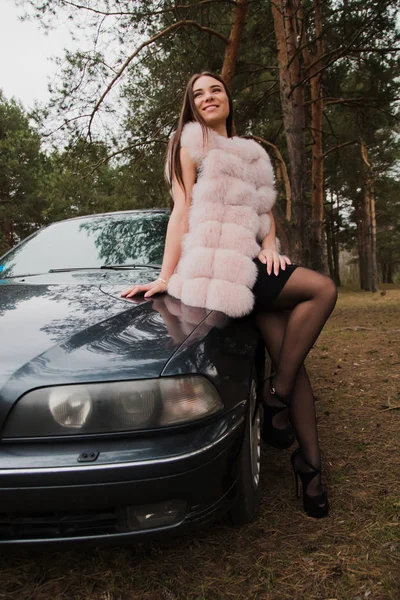 Retrato de una chica muy hermosa en un bosque vestida de piel en un coche — Foto de Stock