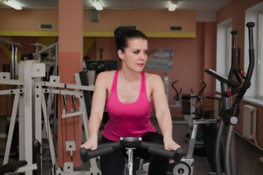Güzel kız bir fitness kulübünde sabit bir bisiklet üzerinde egzersiz