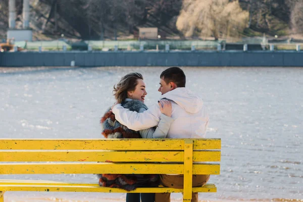 Happy couple in love hugging and sharing emotions, holding hands on a bench by the river — Stock Photo, Image