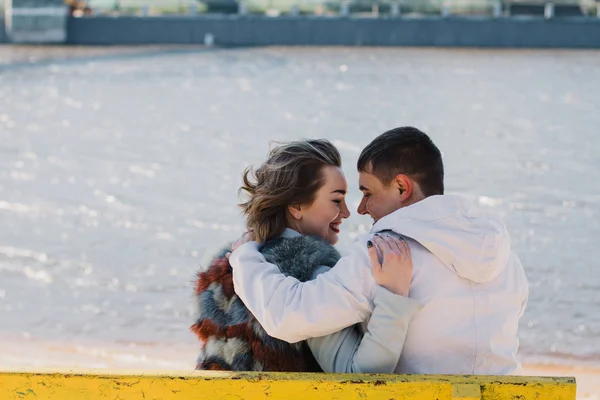 Happy couple in love hugging and sharing emotions, holding hands on a bench by the river — Stock Photo, Image