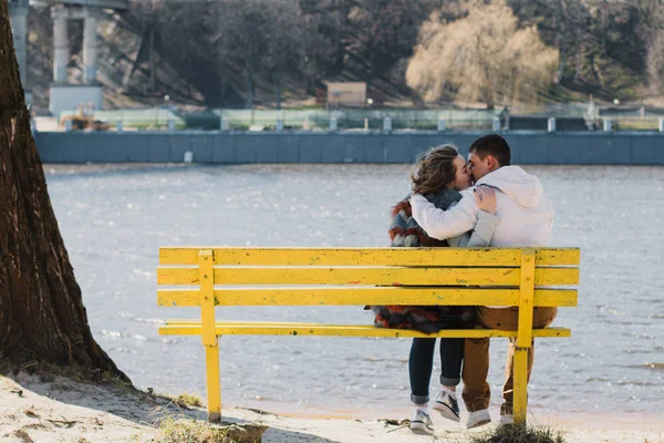 Happy couple in love hugging and sharing emotions, holding hands on a bench by the river — Stock Photo, Image