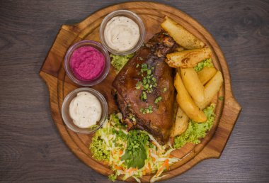 Kızarmış domuz bacak baget, yaban domuzu diz sebzeli kırmızı ve sarı domates, sarımsak, maydanoz ve fesleğen ve patates ahşap arka plan üzerinde