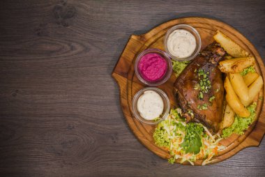 Kızarmış domuz bacak baget, yaban domuzu diz sebzeli kırmızı ve sarı domates, sarımsak, maydanoz ve fesleğen ve patates ahşap arka plan üzerinde