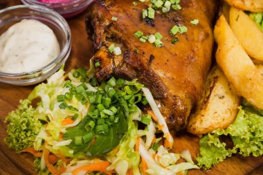 Kızarmış domuz bacak baget, yaban domuzu diz sebzeli kırmızı ve sarı domates, sarımsak, maydanoz ve fesleğen ve patates ahşap arka plan üzerinde