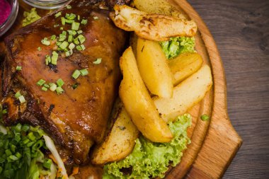 Kızarmış domuz bacak baget, yaban domuzu diz sebzeli kırmızı ve sarı domates, sarımsak, maydanoz ve fesleğen ve patates ahşap arka plan üzerinde