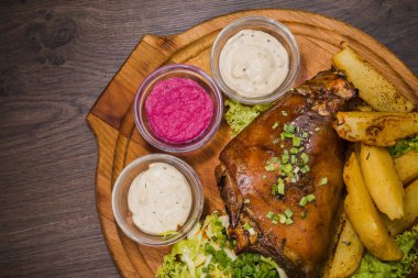 Kızarmış domuz bacak baget, yaban domuzu diz sebzeli kırmızı ve sarı domates, sarımsak, maydanoz ve fesleğen ve patates ahşap arka plan üzerinde