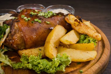 Kızarmış domuz bacak baget, yaban domuzu diz sebzeli kırmızı ve sarı domates, sarımsak, maydanoz ve fesleğen ve patates ahşap arka plan üzerinde