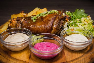 Kızarmış domuz bacak baget, yaban domuzu diz sebzeli kırmızı ve sarı domates, sarımsak, maydanoz ve fesleğen ve patates ahşap arka plan üzerinde