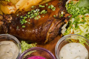 Kızarmış domuz bacak baget, yaban domuzu diz sebzeli kırmızı ve sarı domates, sarımsak, maydanoz ve fesleğen ve patates ahşap arka plan üzerinde