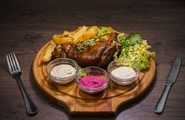 Kızarmış domuz bacak baget, yaban domuzu diz sebzeli kırmızı ve sarı domates, sarımsak, maydanoz ve fesleğen ve patates ahşap arka plan üzerinde