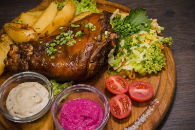 Kızarmış domuz bacak baget, yaban domuzu diz sebzeli kırmızı ve sarı domates, sarımsak, maydanoz ve fesleğen ve patates ahşap arka plan üzerinde