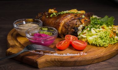 Kızarmış domuz bacak baget, yaban domuzu diz sebzeli kırmızı ve sarı domates, sarımsak, maydanoz ve fesleğen ve patates ahşap arka plan üzerinde