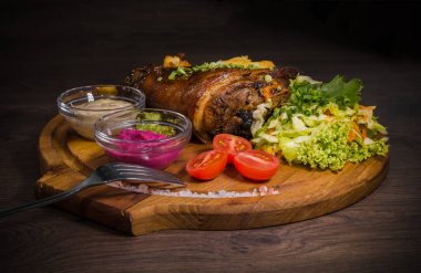 Kızarmış domuz bacak baget, yaban domuzu diz sebzeli kırmızı ve sarı domates, sarımsak, maydanoz ve fesleğen ve patates ahşap arka plan üzerinde