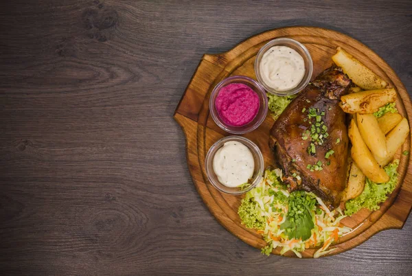 Kızarmış domuz bacak baget, yaban domuzu diz sebzeli kırmızı ve sarı domates, sarımsak, maydanoz ve fesleğen ve patates ahşap arka plan üzerinde