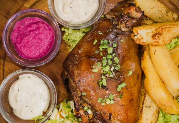 Kızarmış domuz bacak baget, yaban domuzu diz sebzeli kırmızı ve sarı domates, sarımsak, maydanoz ve fesleğen ve patates ahşap arka plan üzerinde