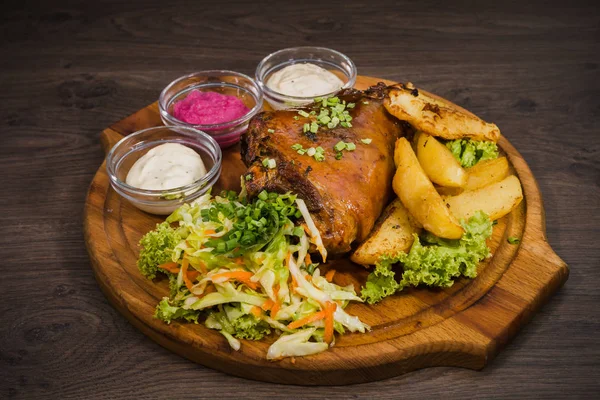 Kızarmış domuz bacak baget, yaban domuzu diz sebzeli kırmızı ve sarı domates, sarımsak, maydanoz ve fesleğen ve patates ahşap arka plan üzerinde