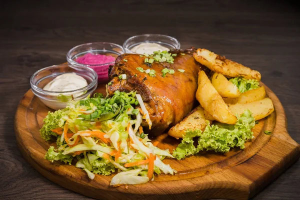 Kızarmış domuz bacak baget, yaban domuzu diz sebzeli kırmızı ve sarı domates, sarımsak, maydanoz ve fesleğen ve patates ahşap arka plan üzerinde