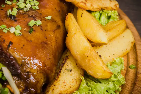 Kızarmış domuz bacak baget, yaban domuzu diz sebzeli kırmızı ve sarı domates, sarımsak, maydanoz ve fesleğen ve patates ahşap arka plan üzerinde