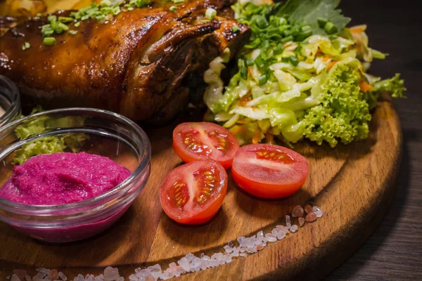 Kızarmış domuz bacak baget, yaban domuzu diz sebzeli kırmızı ve sarı domates, sarımsak, maydanoz ve fesleğen ve patates ahşap arka plan üzerinde