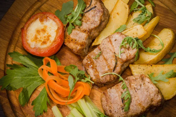 Three pork steaks with fried potatoes and vegetables on a wooden background — Stock Photo, Image