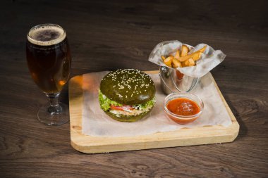Yeşil burger patates kızartması ve domates sosu bir bardak bira ile ahşap bir stand