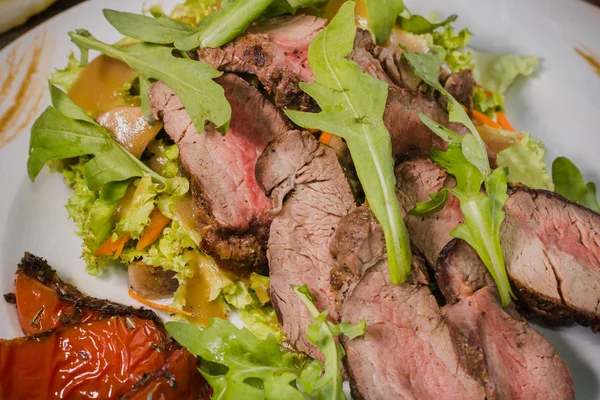 Roasted meat with blood in a cut with vegetables on a wooden background — Stock Photo, Image