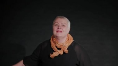 Elli yaşında bir kadın siyah bir arka planda hula hoop çeviriyor..