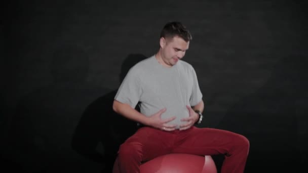 Jongeman met een maag op een gymnastiekbal. — Stockvideo
