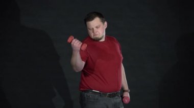 Genç bir adam beceriksizce dambıllarla antrenman yapıyor..