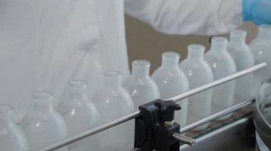 Enjeksiyon şişelerini yıkamak ve dezenfekte etmek için konveyördeki kadın bilim adamı..