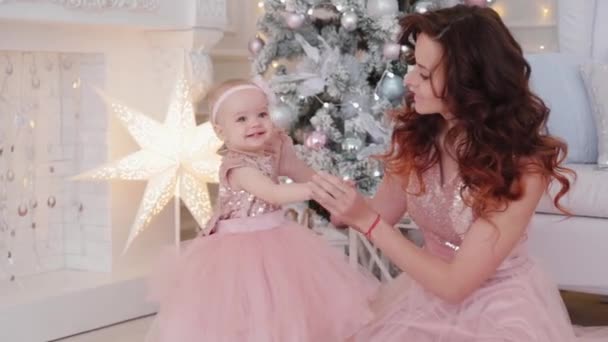 Beautiful mother with a one-year-old daughter in beautiful dresses and New Years decor. New Year 2020. — Stock Video