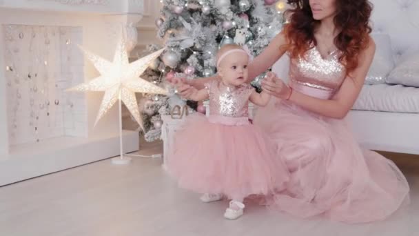 Bela mãe com uma filha de um ano de idade em belos vestidos e decoração de Ano Novo. Ano Novo 2020 . — Vídeo de Stock