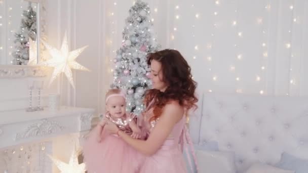 Beautiful mother with a one-year-old daughter in beautiful dresses and New Years decor. New Year 2020. — Stock Video