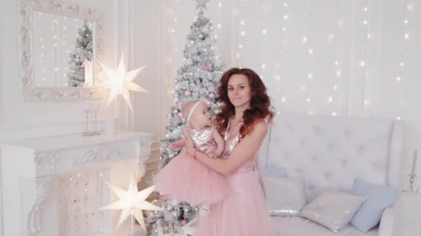 Beautiful mother with a one-year-old daughter in beautiful dresses and New Years decor. New Year 2020. — Stock Video