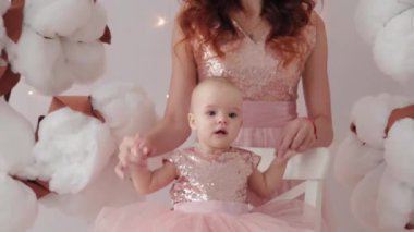 Güzel bir anne ve bir yaşında bir kızı yapay pamuk ve parlak bir duvarın yanında bir fotoğraf stüdyosunda..