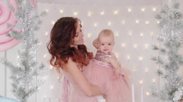 Schöne Mutter mit einer einjährigen Tochter in schönen Kleidern und Silvesterdekor. Neues Jahr 2020. — Stockvideo