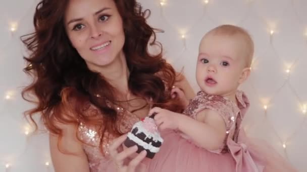 Gyönyörű anya egy egyéves kislánnyal, gyönyörű ruhákban és szilveszteri dekorációban. Új év 2020. — Stock videók