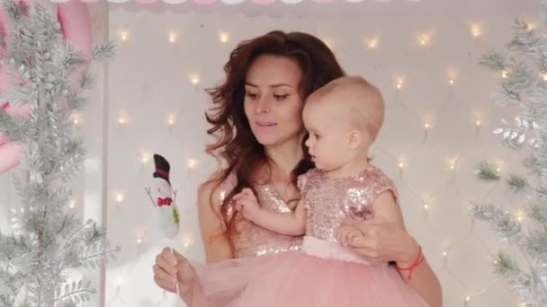 Beautiful mother with a one-year-old daughter in beautiful dresses and New Years decor. New Year 2020. — Stock Video