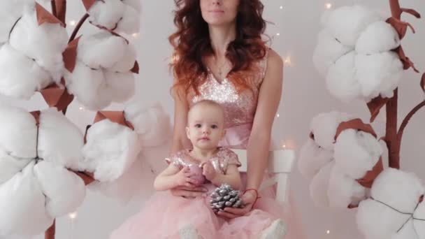 Hermosa madre con una hija de un año en un estudio fotográfico cerca de algodón artificial y una pared luminosa . — Vídeos de Stock