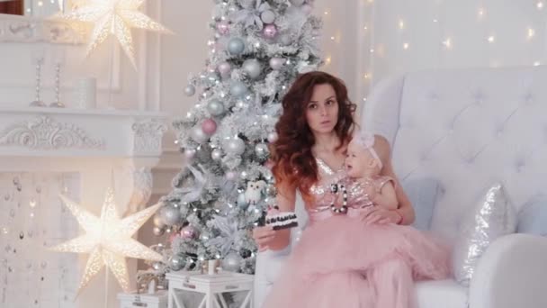 Beautiful mother with a one-year-old daughter in beautiful dresses and New Years decor. New Year 2020. — Stock Video