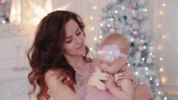 Vacker mor med en ettårig dotter i vackra klänningar och nyårsinredning. Nytt år 2020. — Stockvideo